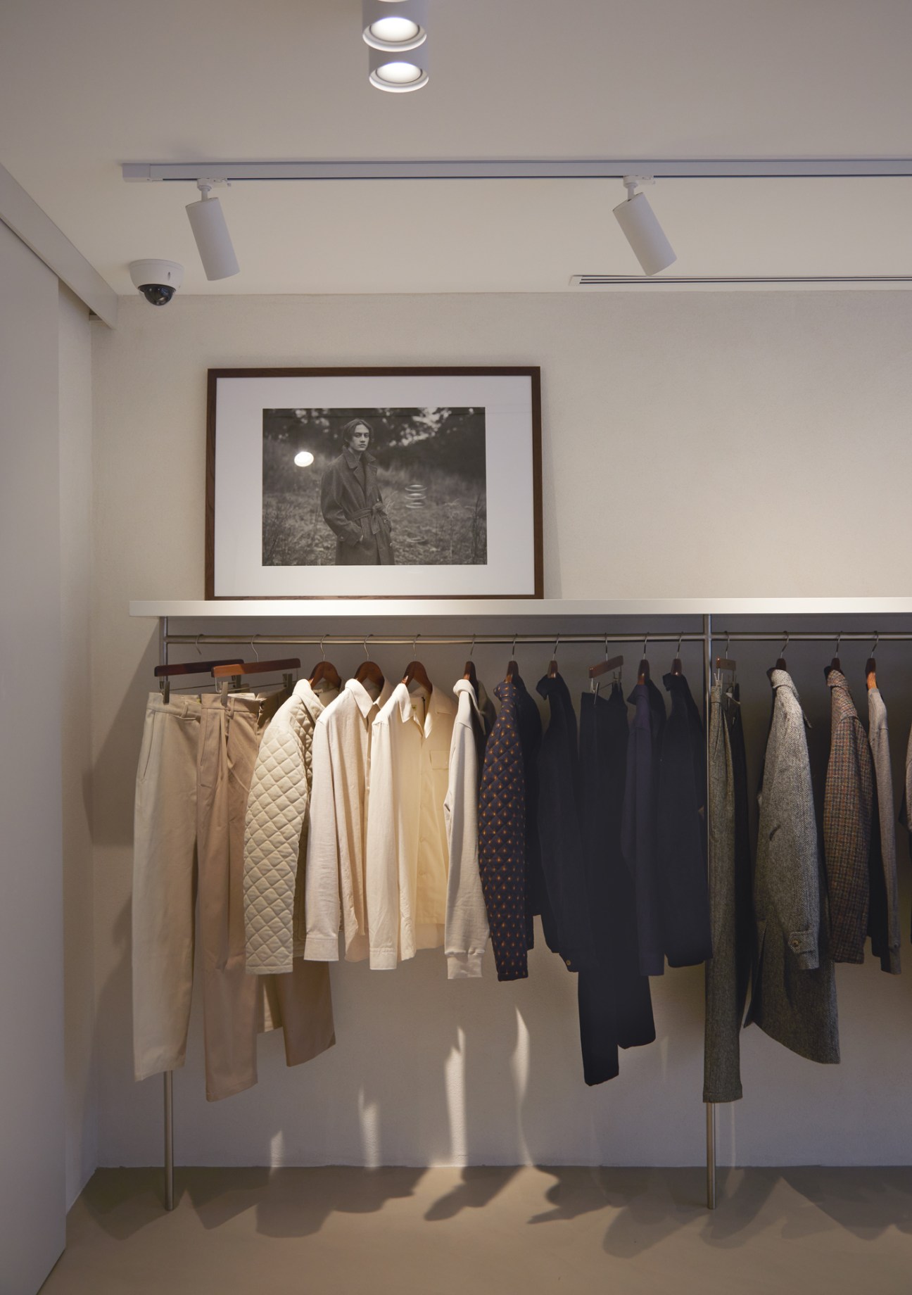 Clothing hanging on rail in minimalist store interior with white walls and track lighting