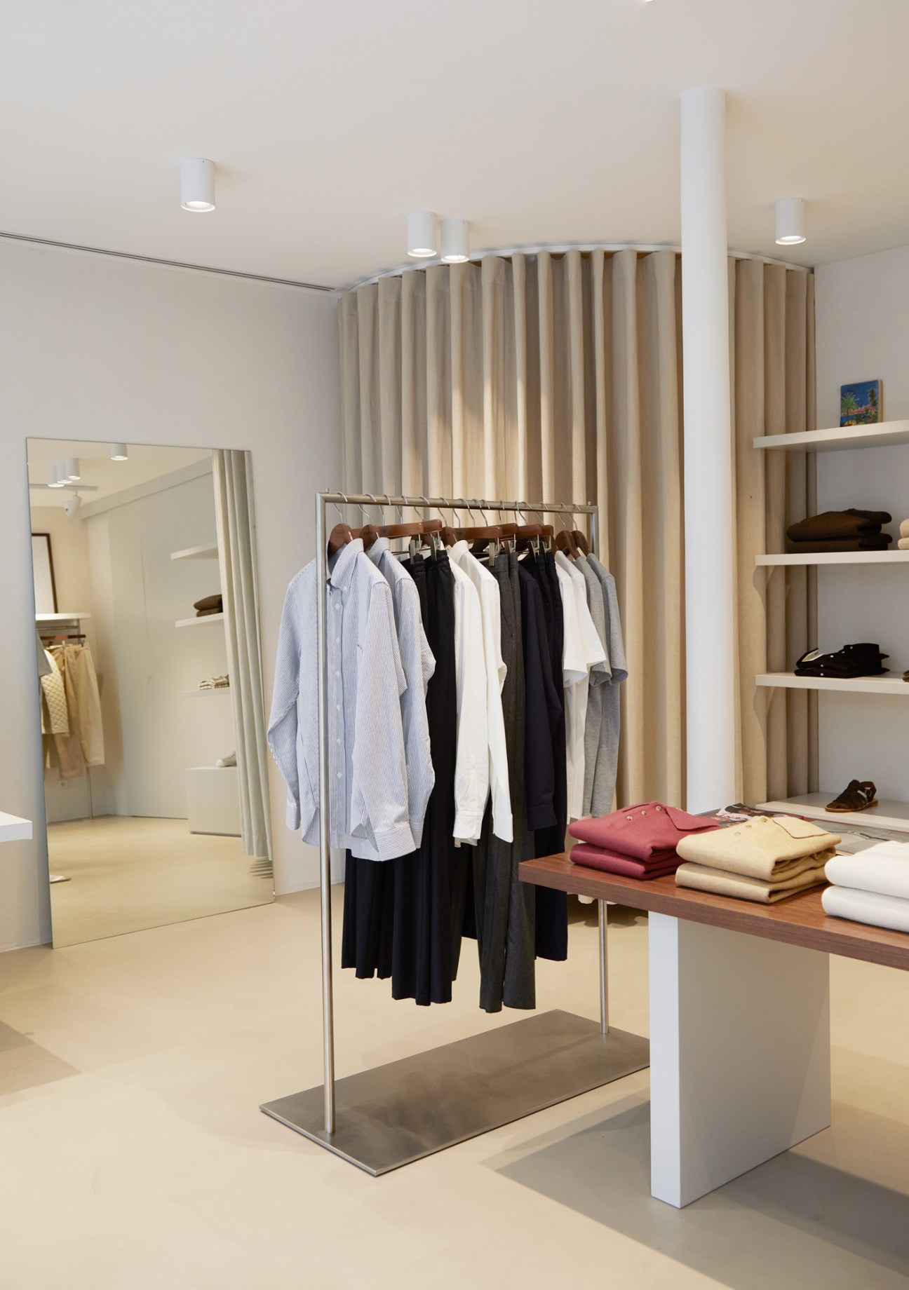 Wide view of De Bonne Facture store interior with clothing rack, folded garments on table, and neutral minimalist design
