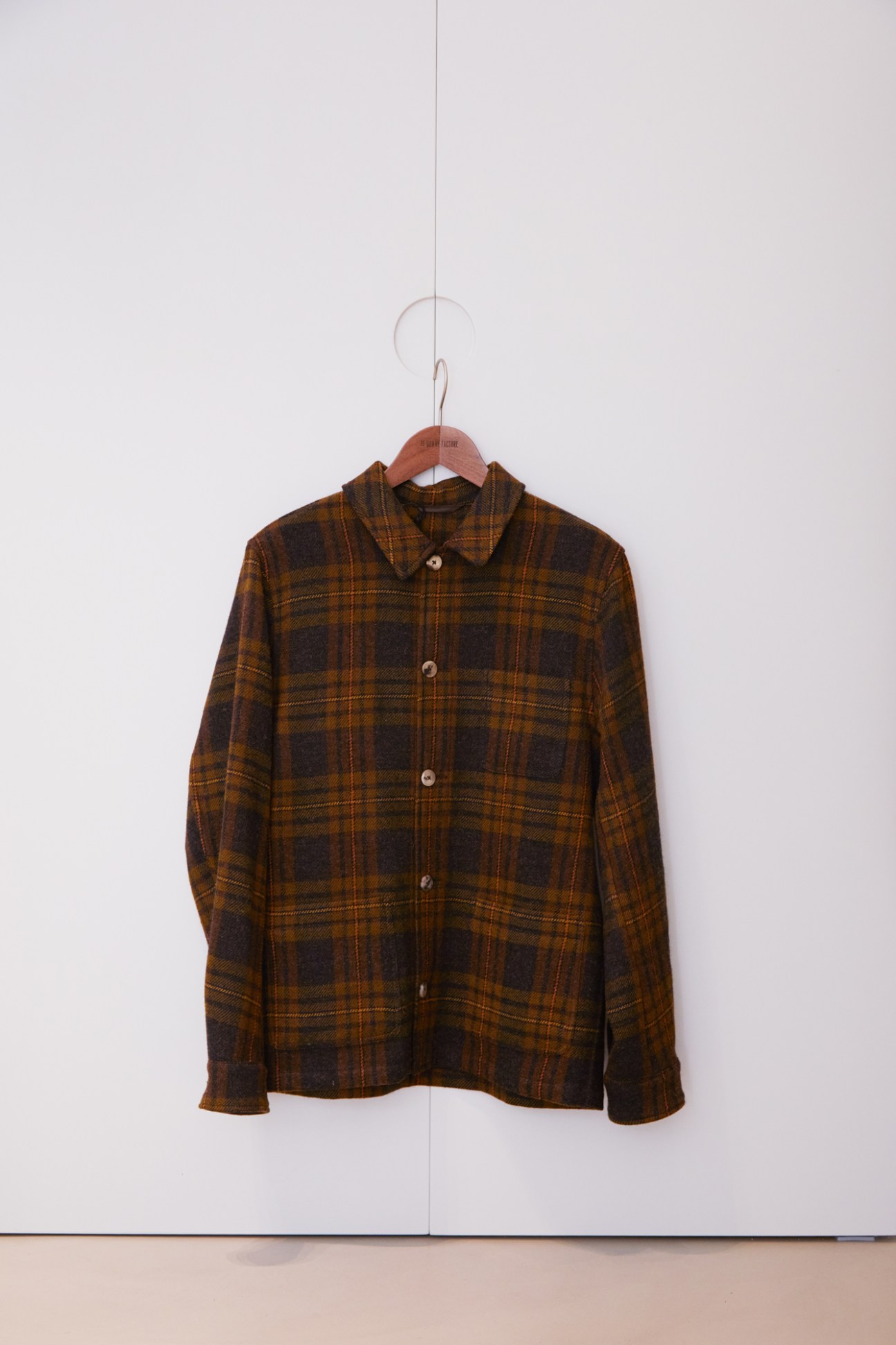 Brown plaid flannel shirt hanging on wooden hanger against white wall