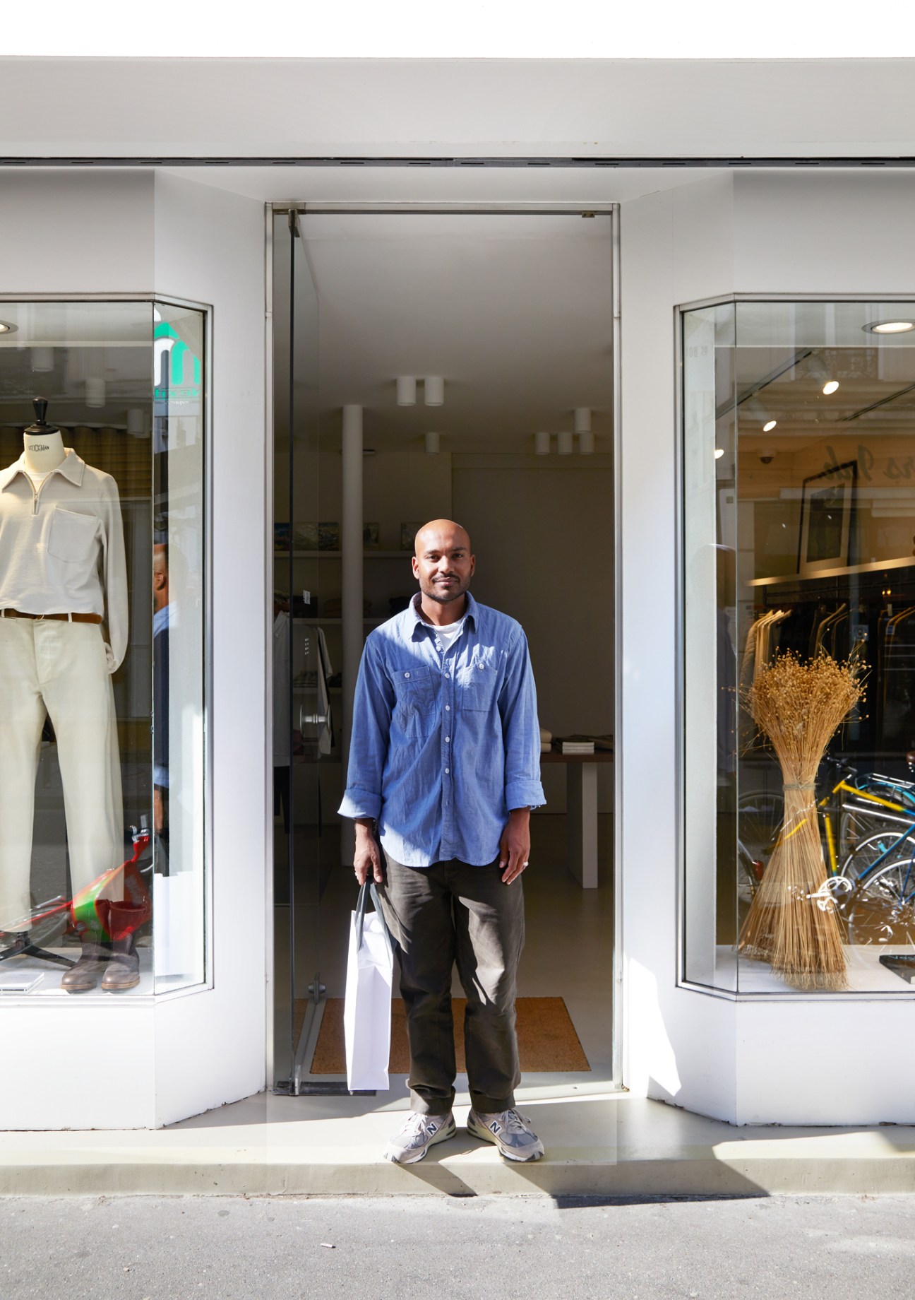 Man in blue shirt standing in doorway of De Bonne Facture store with clothing displays in windows