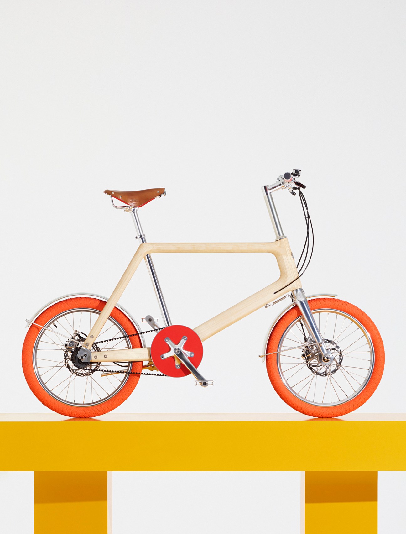 Hermès Ash Wood Bike with cream-colored wooden frame, brown leather saddle, orange tires, and red chainring.