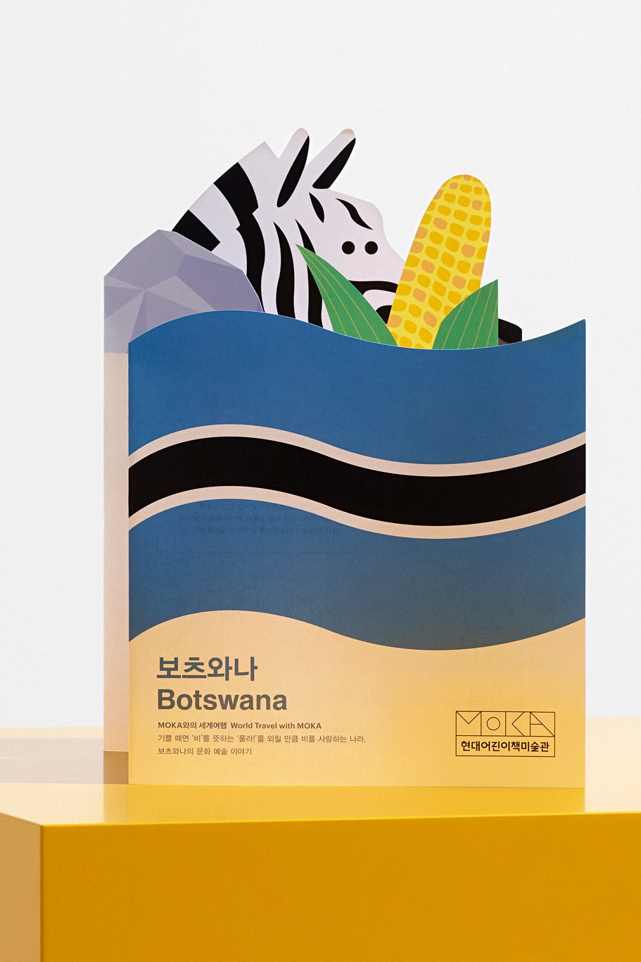 Colorful illustrated book cover for 'World Travel with Moka' featuring a zebra and corn among layered blue and sand-colored waves.