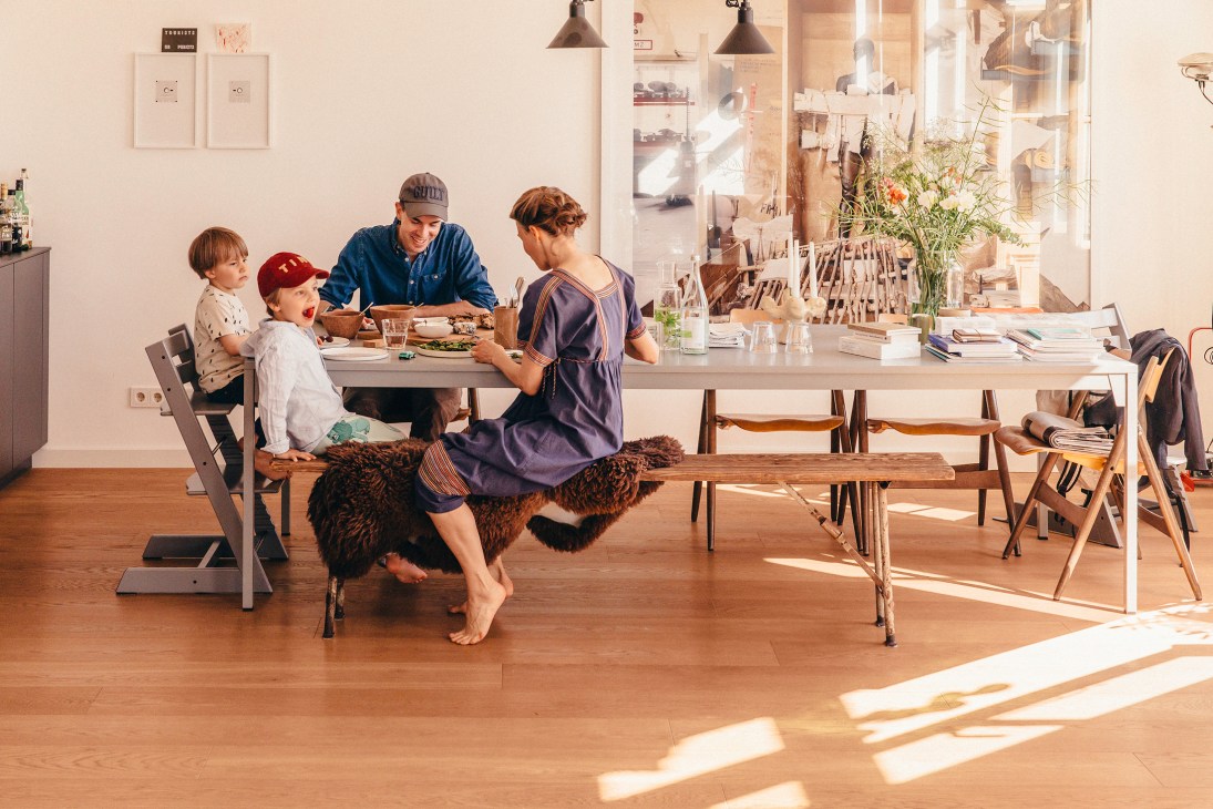 Family of four sitting around white dining table in modern home with wooden floors and large windows