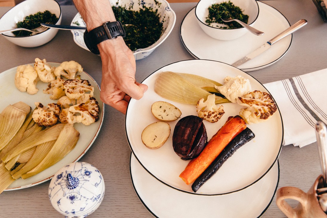 Grilled root vegetables including carrots and parsnips with leafy greens on white plates