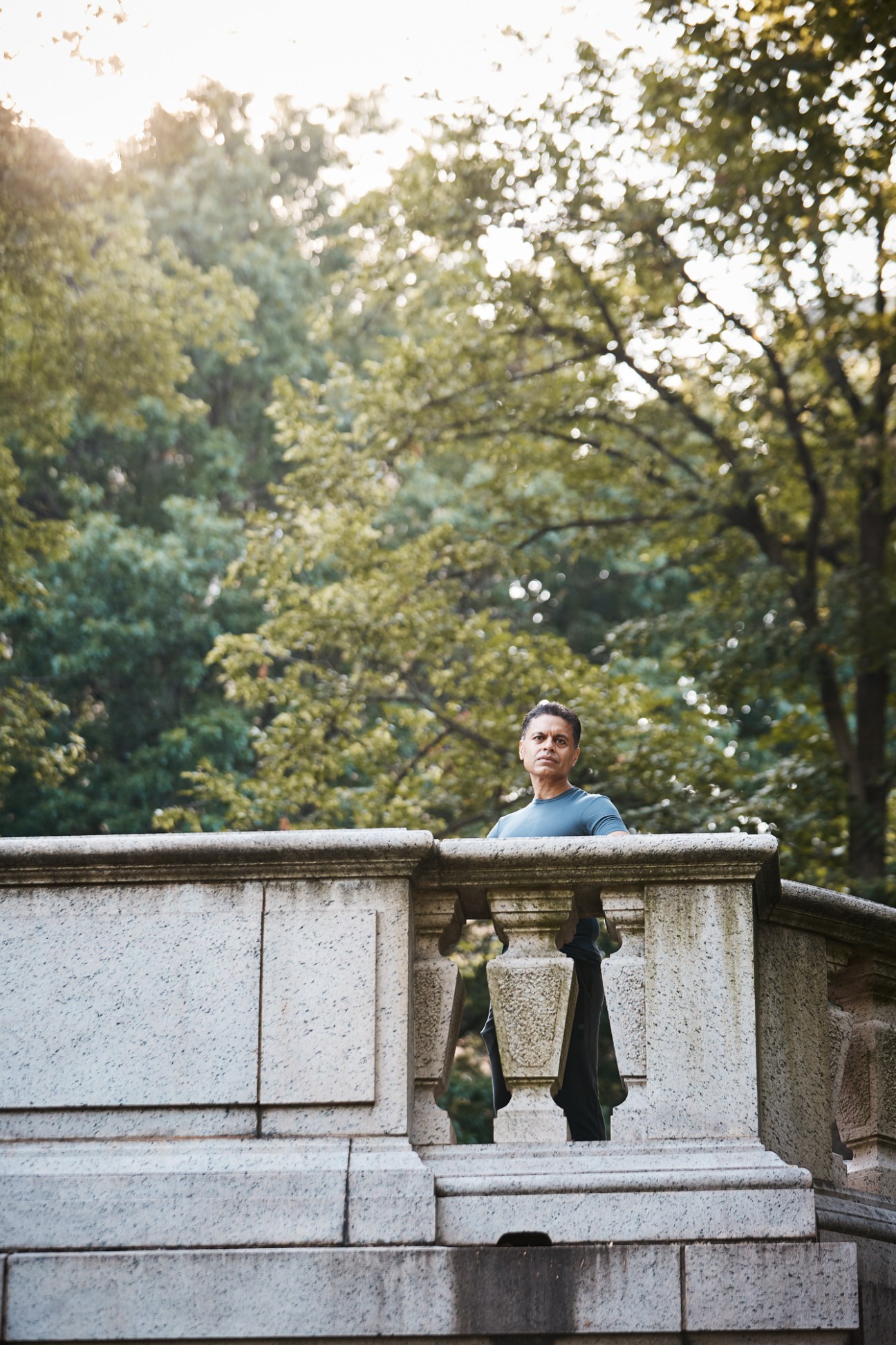 Fareed Zakaria standing behind ornate stone balustrade in park with leafy trees in background