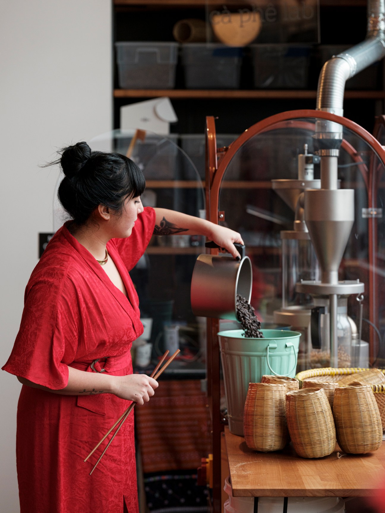 Woman in red shirt pouring roasted coffee beans from a scoop into a green bucket at Hello Em café in Seattle's Little Saigon Creative hub.