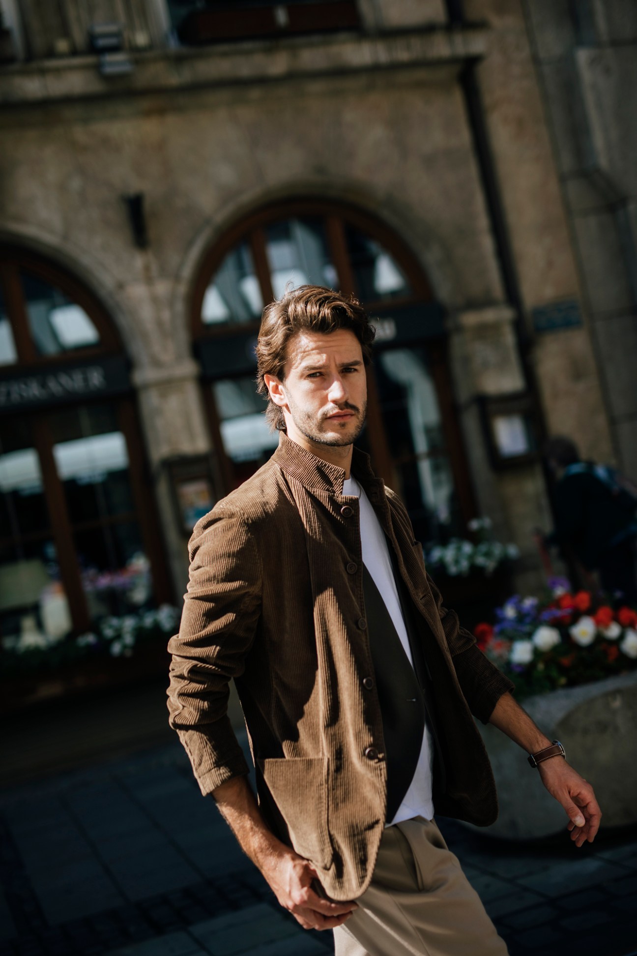 Man in brown corduroy suit walking confidently past historic European architecture with arched windows