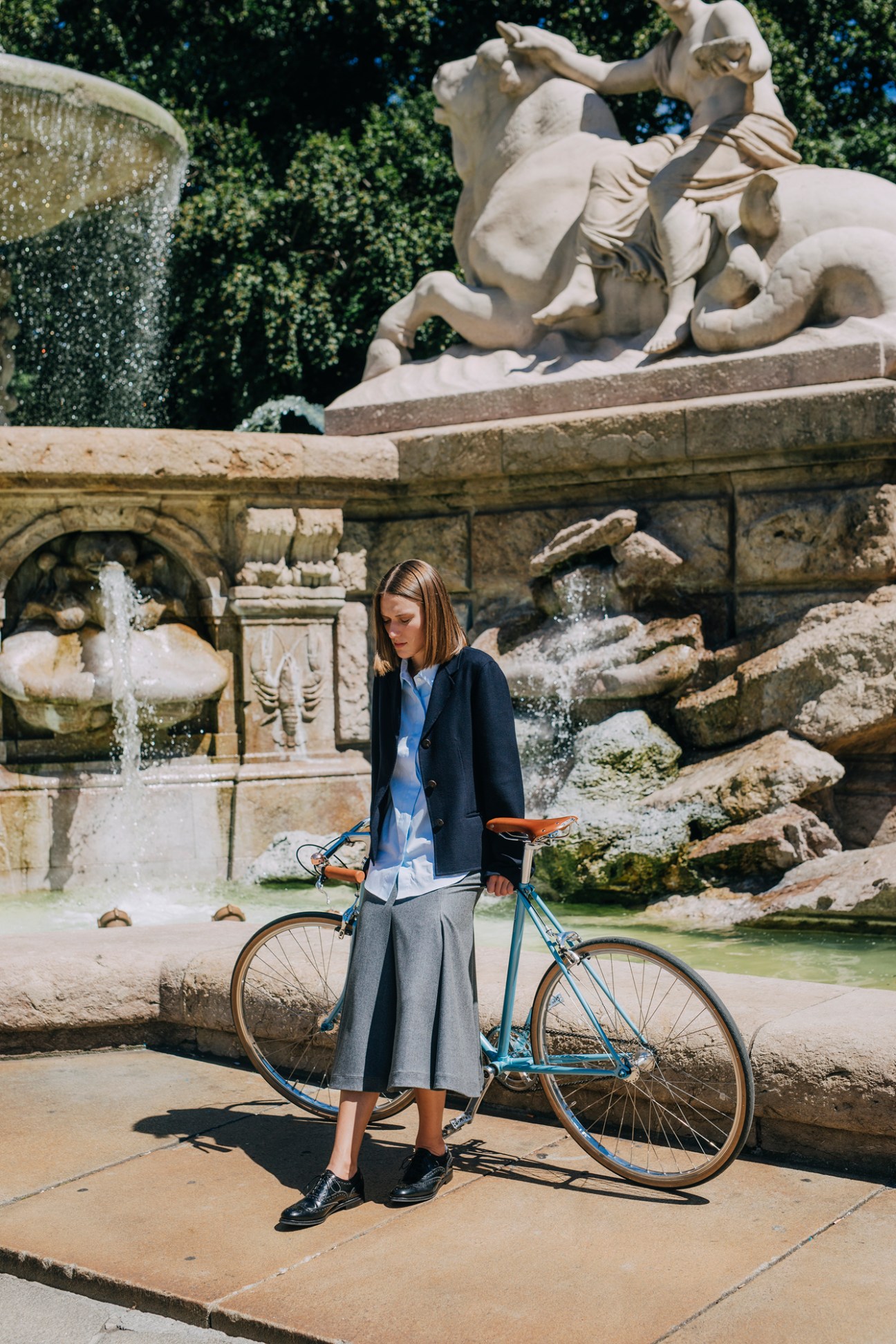 Woman with bicycle standing by ornate baroque fountain with cascading water and classical stone sculptures