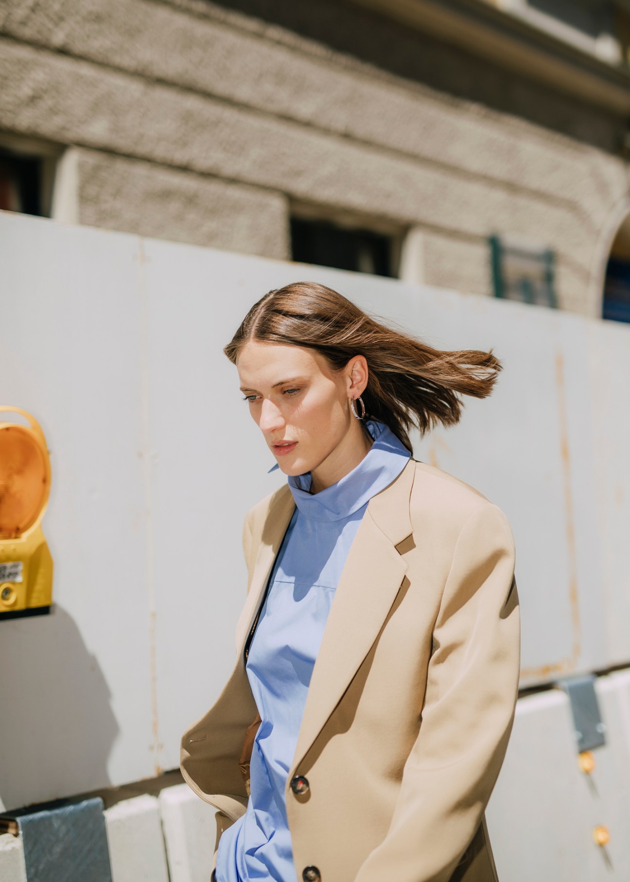 Woman in beige blazer and light blue blouse with hair in motion walking outdoors