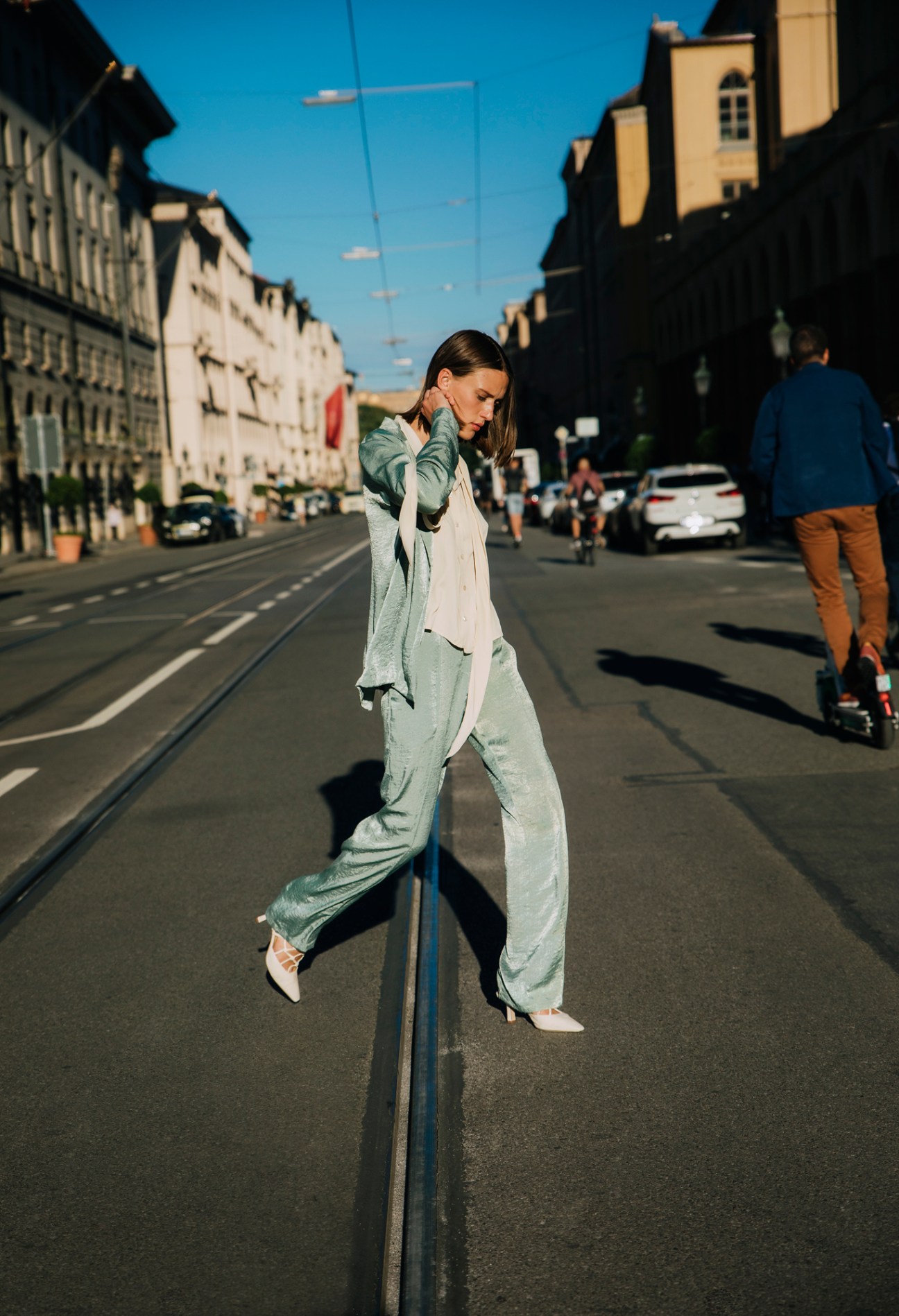 Woman in mint green outfit walking along tram tracks on a Munich street with historic European buildings
