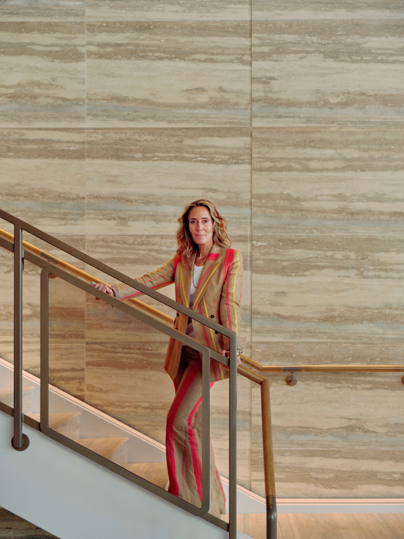 Portrait of British interior designer Tara Bernerd standing on modern staircase wearing striped blazer
