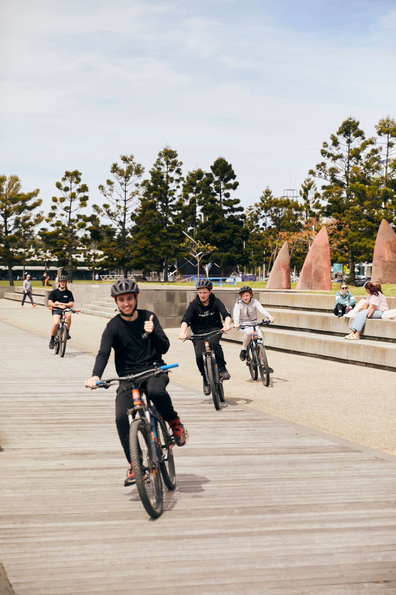Multiple cyclists riding on a wooden boardwalk waterfront promenade in Geelong, Australia.