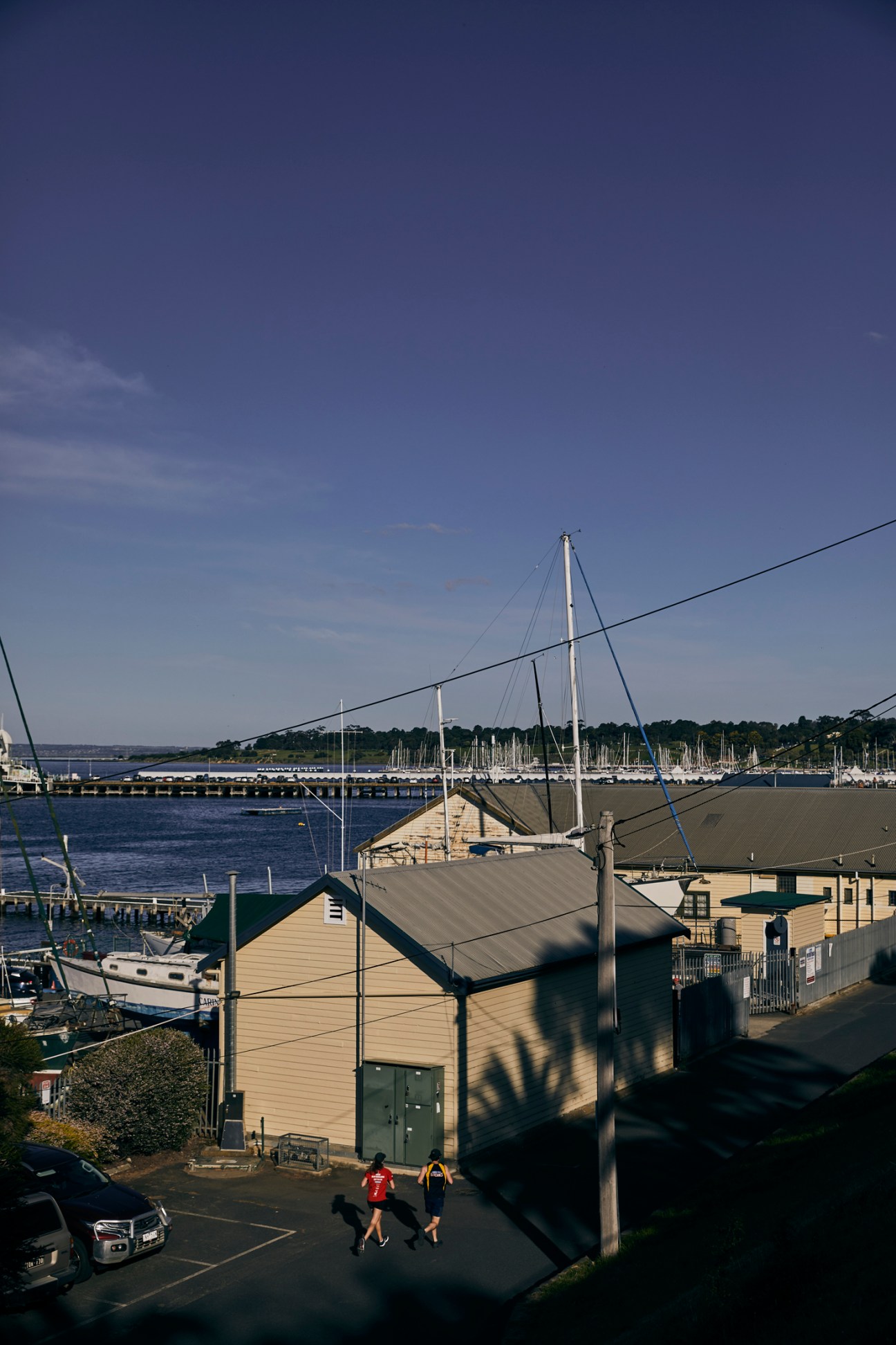 Geelong waterfront with sailboats moored in the marina and people jogging on the esplanade.
