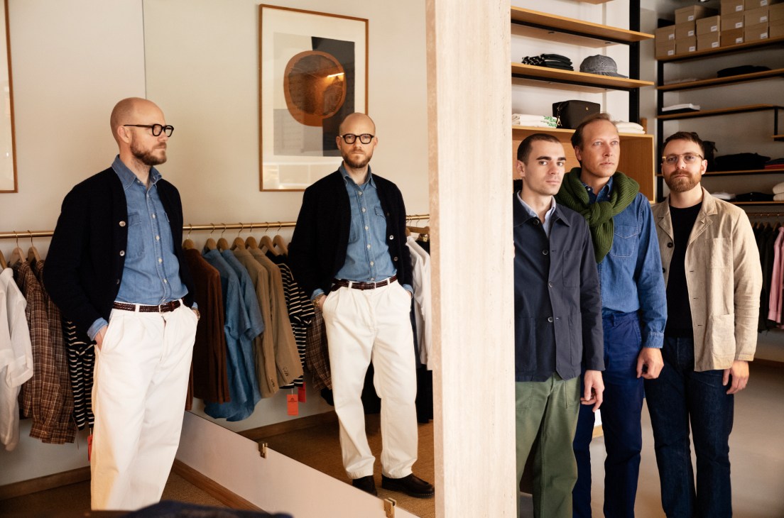 Four men standing in a modern menswear store with clothing racks and shelving displaying merchandise in background