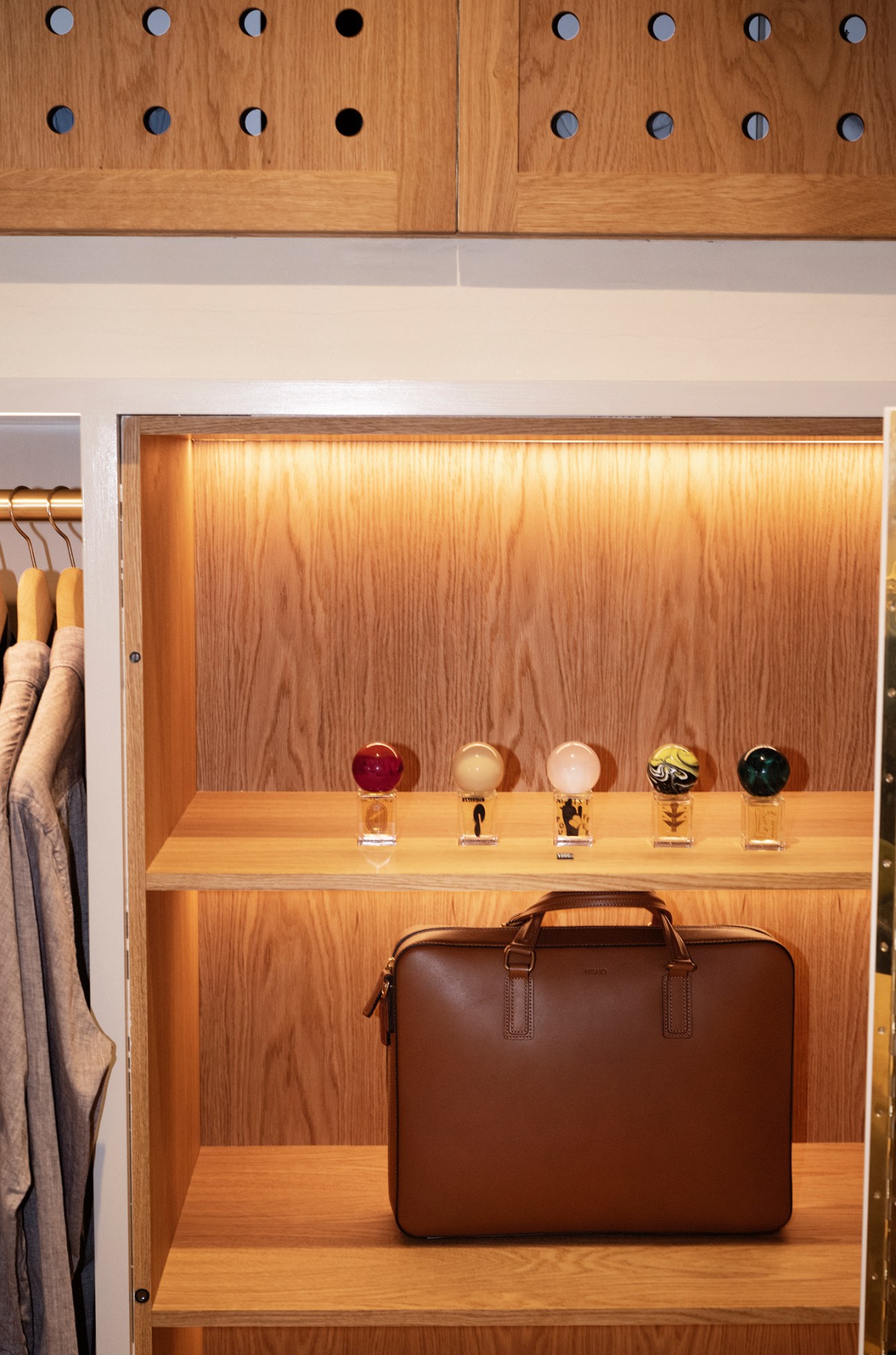Brown leather bag and colorful fragrance bottles displayed on wooden shelf in menswear store