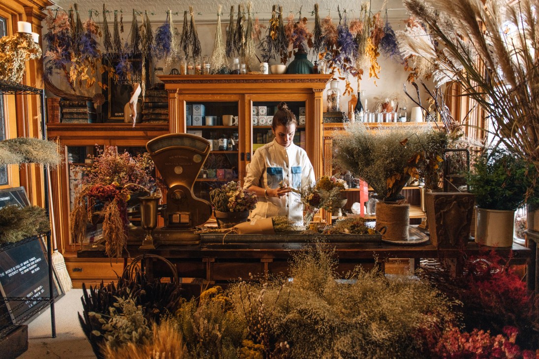 Florist arranging dried flowers and botanicals in a rustic shop interior at the Quiet Botanist