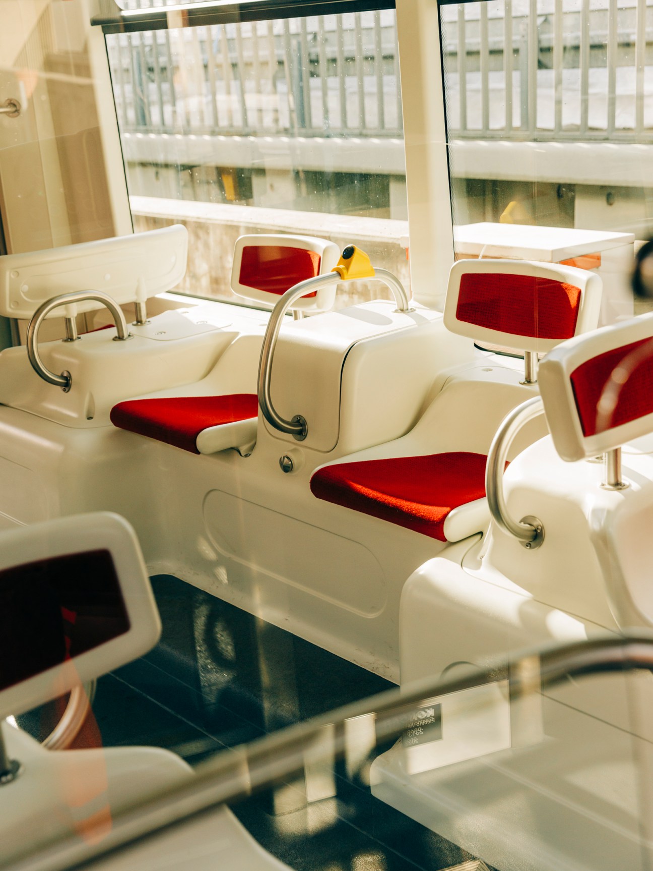 Modern train interior featuring comfortable red upholstered seats with white plastic frames