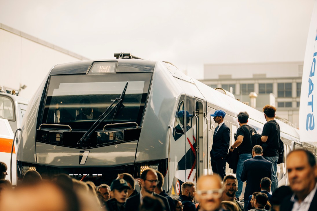 Crowded trade fair with people examining a modern white train under exhibition tent