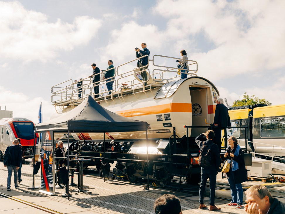 Elevated view of trade fair exhibition with people on platform overlooking trains and displays below