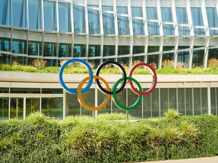 The iconic Olympic rings in blue, yellow, black, green and red displayed outside a modern glass building