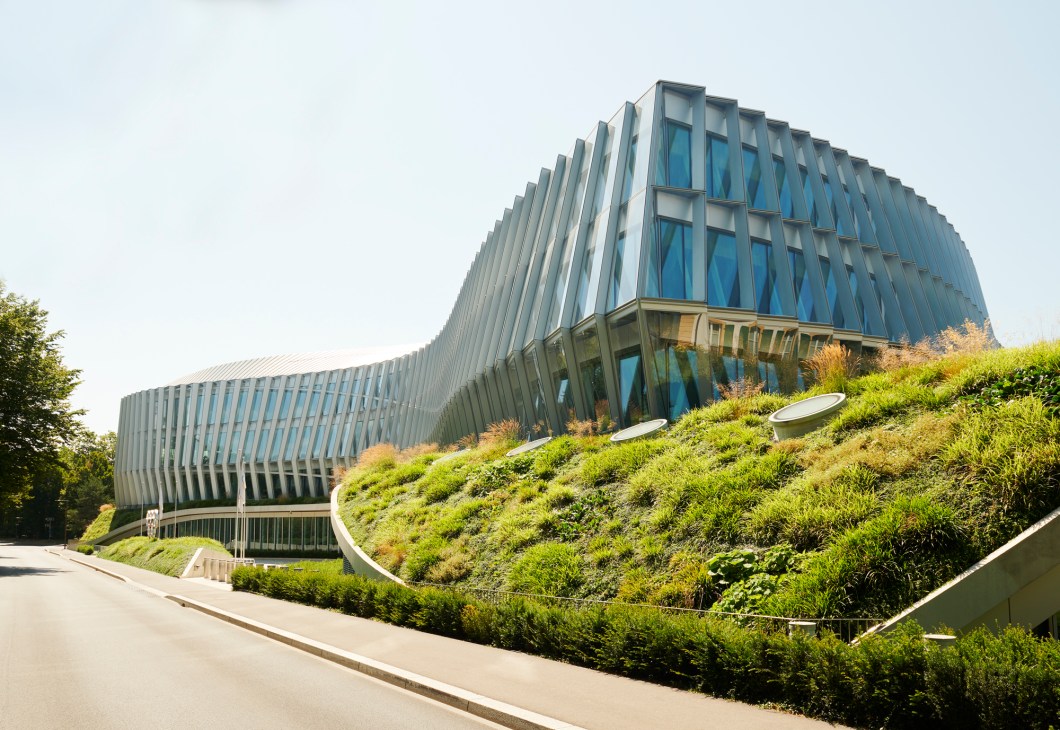Modern curved glass and steel building with vertical metal fins and landscaped green roof against cloudy sky