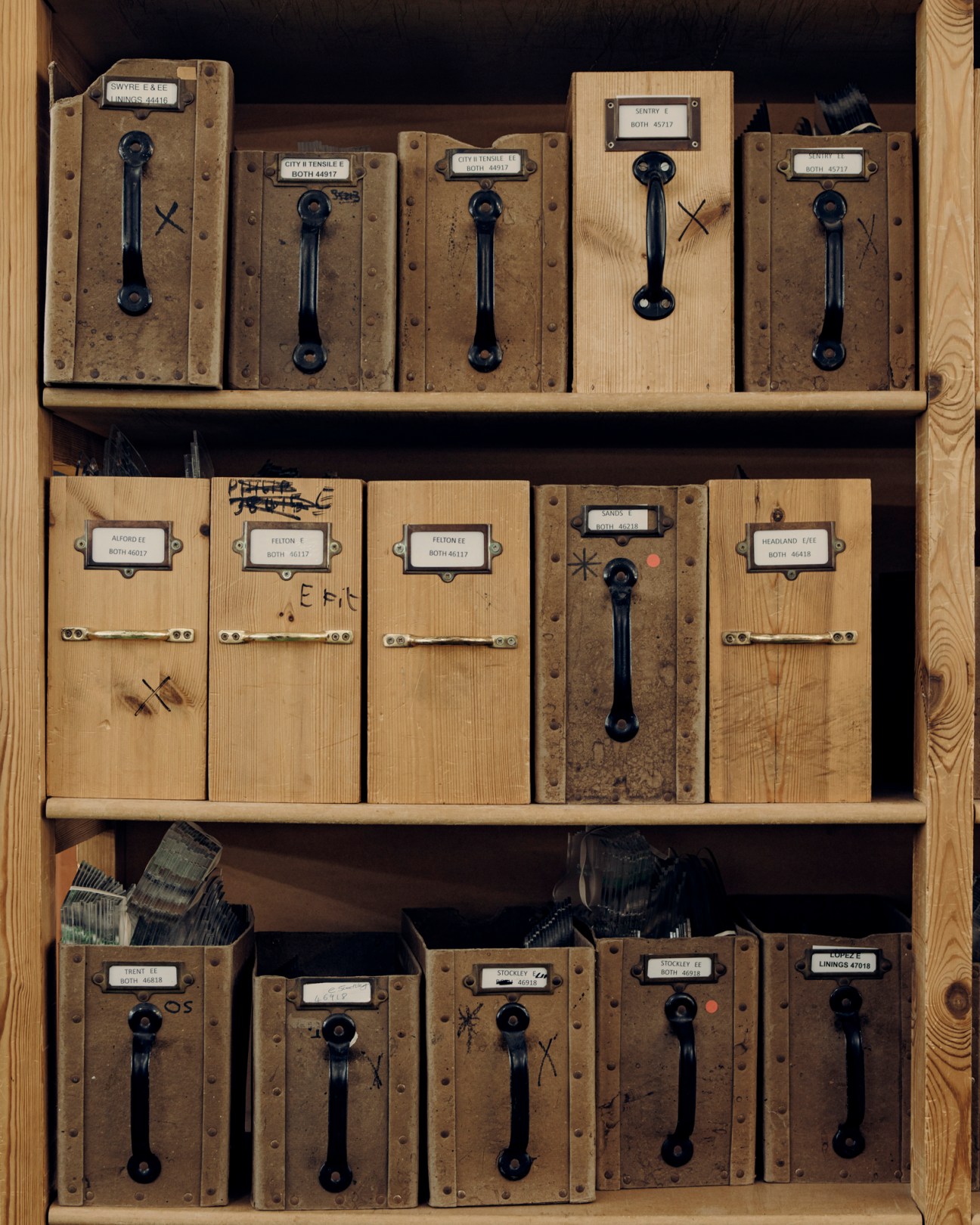 Wooden storage compartments with black handles containing shoe-making tools and materials