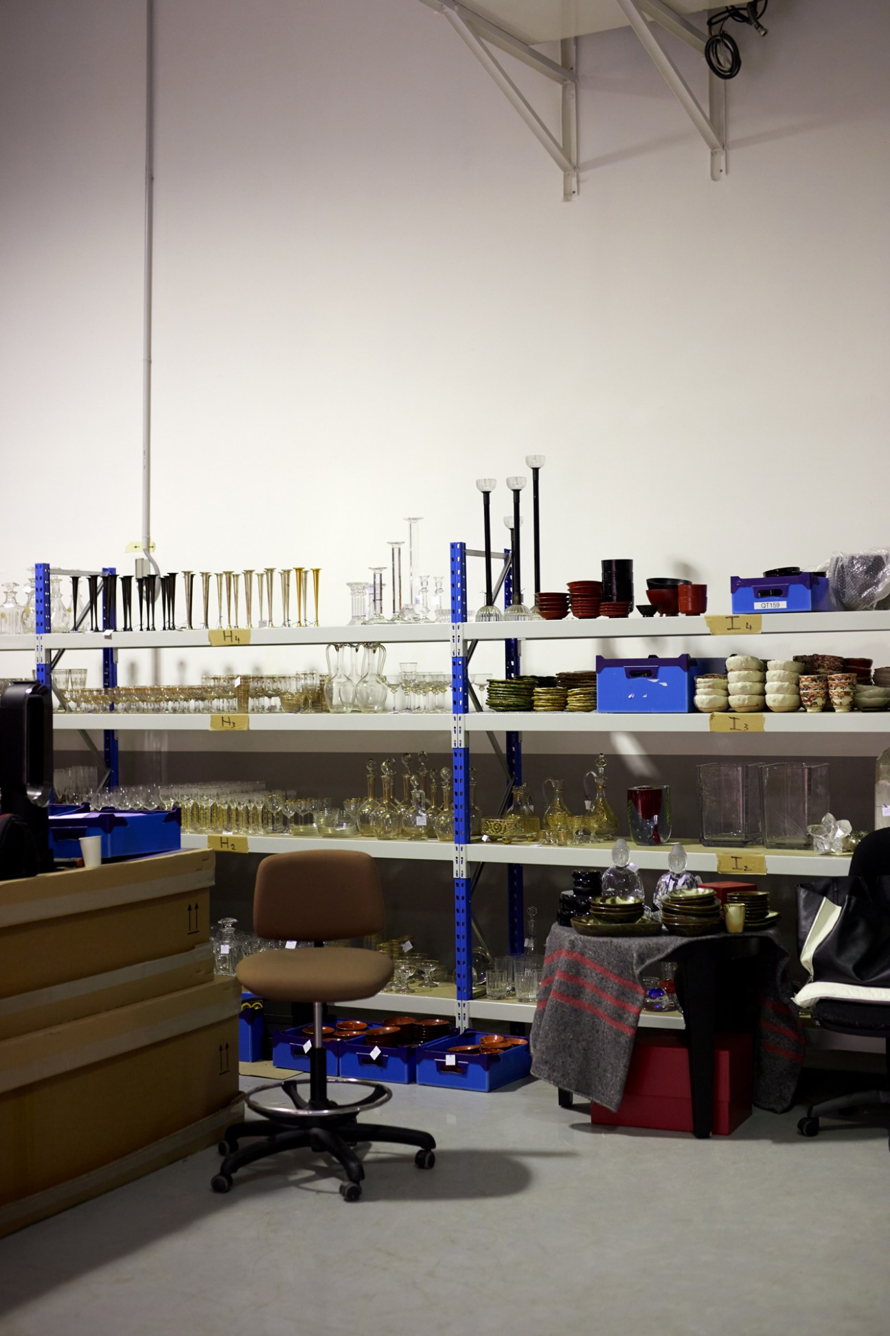 Collection of crystal glassware including candlesticks, carafes and goblets arranged on white shelving in storage facility