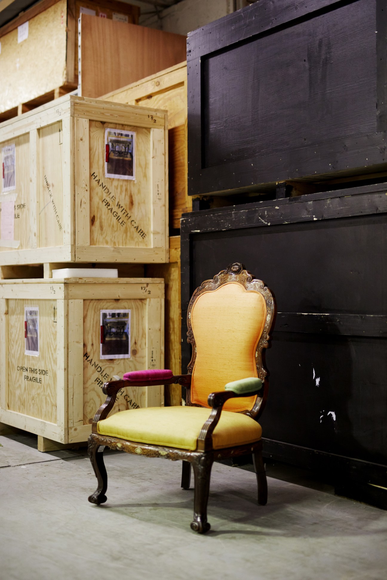 Ornate bergère chair with carved wooden frame and multicolored upholstered seat and back in storage facility