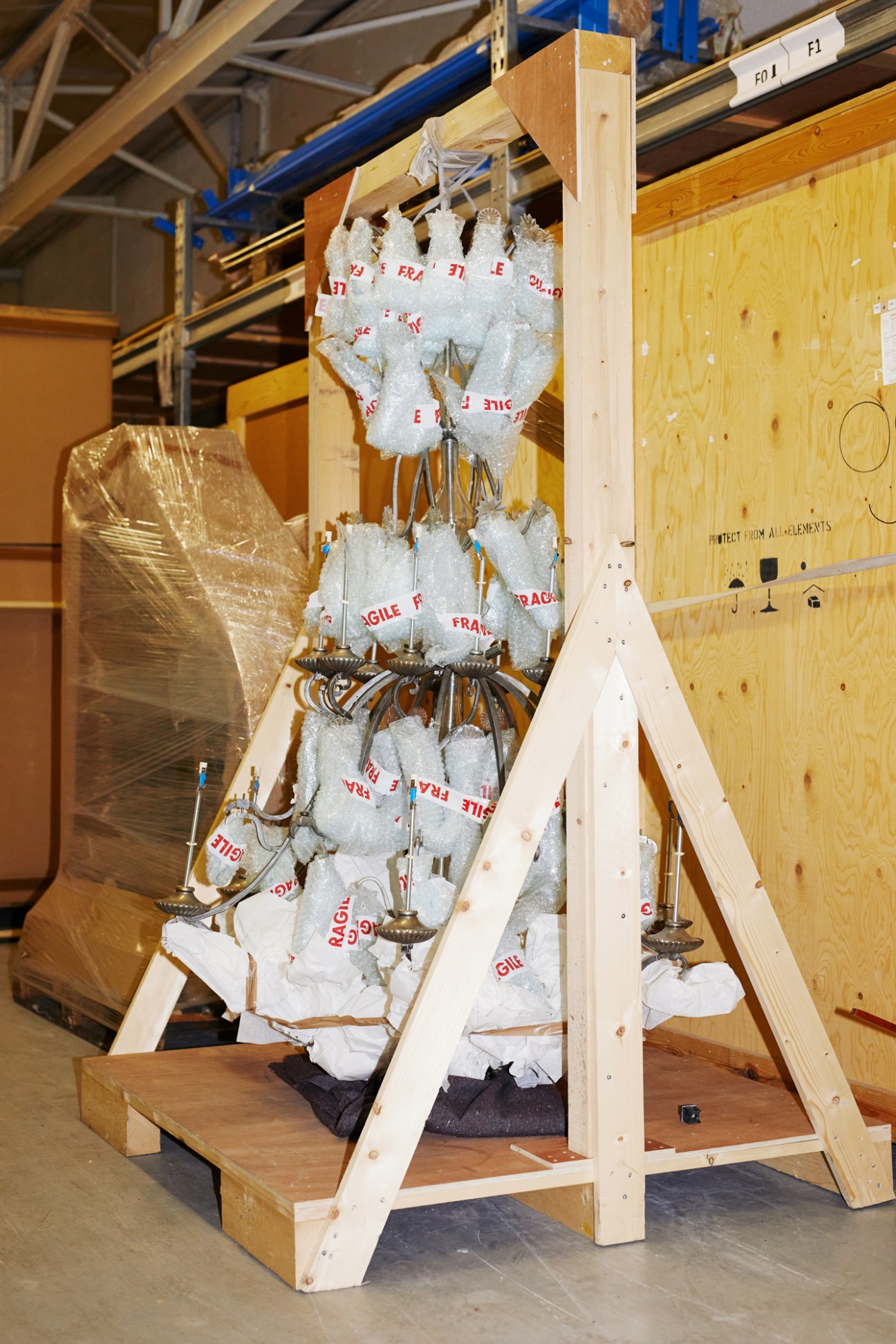 Ornate chandelier carefully wrapped in protective bubble wrap mounted on wooden frame in storage facility