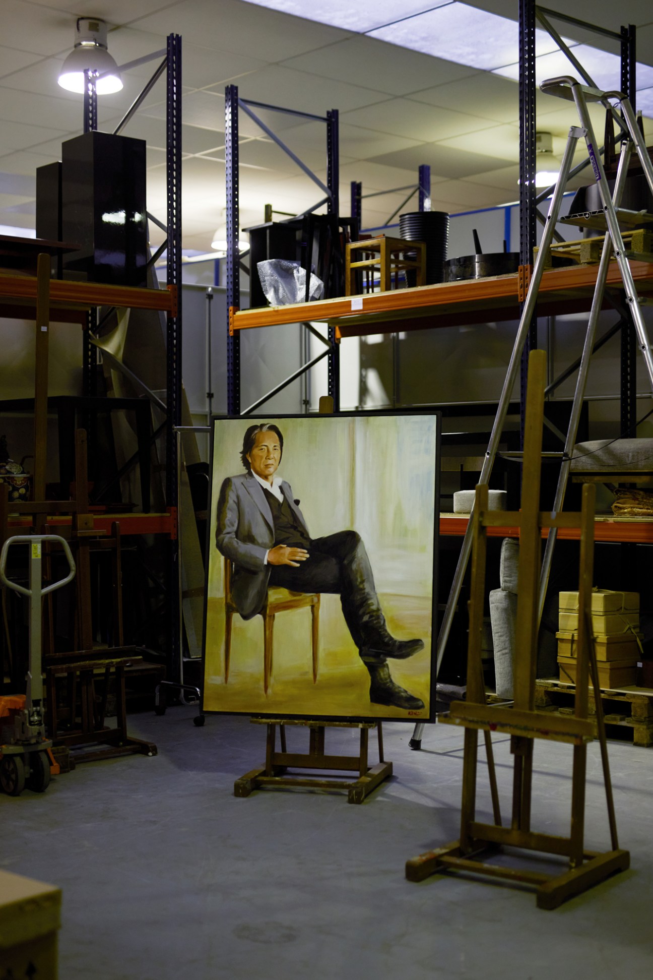 Life-sized self-portrait painting of Kenzo Takada displayed on easel in warehouse storage facility