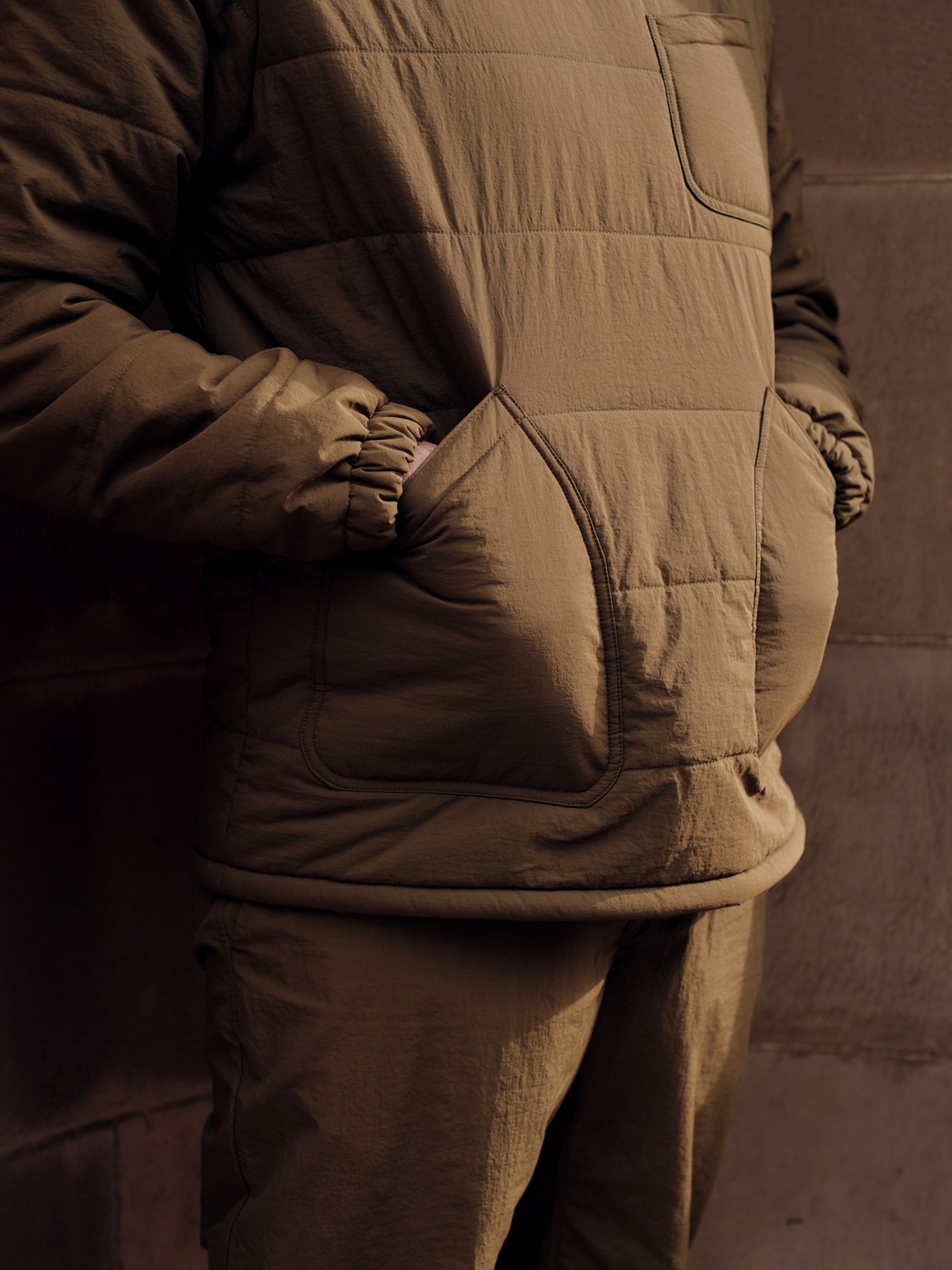 Person wearing beige quilted insulated pullover sitting on wooden stool