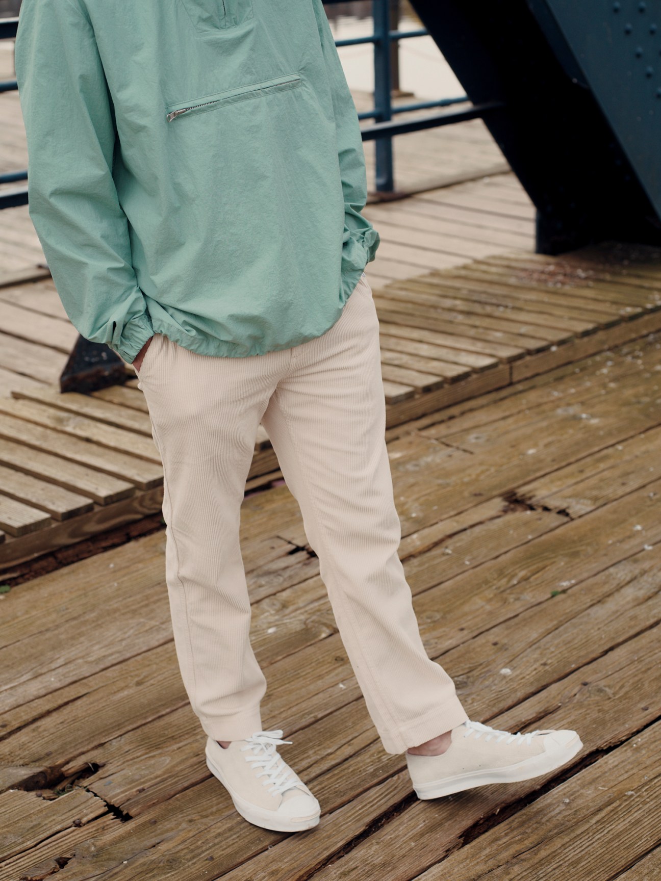 Person wearing sage green pullover and beige corduroy trousers with white sneakers standing on wooden deck