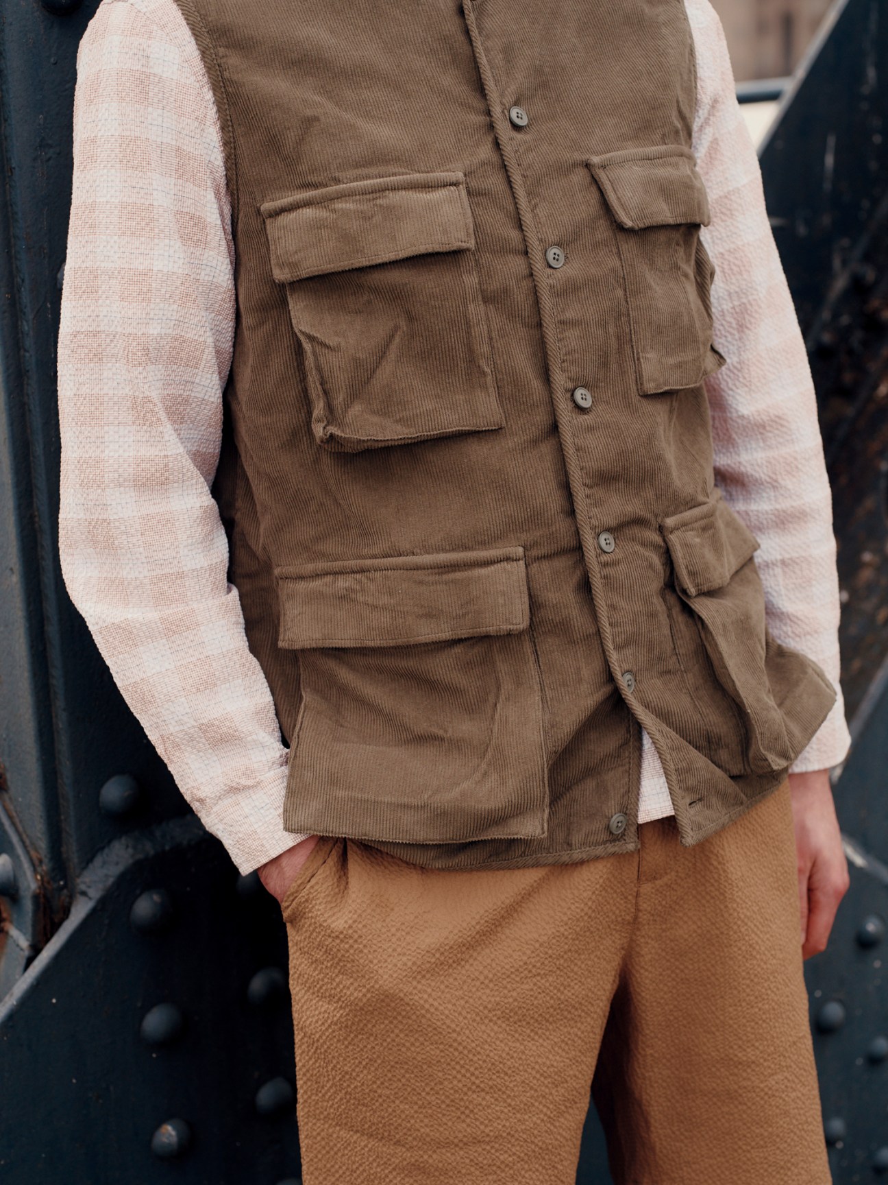 Close-up of a brown corduroy vest with multiple pockets worn over a cream sweater with tan trousers
