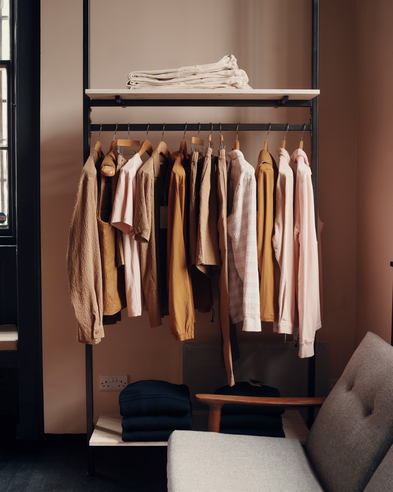 Clothing rack displaying neutral-toned garments including shirts, sweaters and jackets on wooden hangers