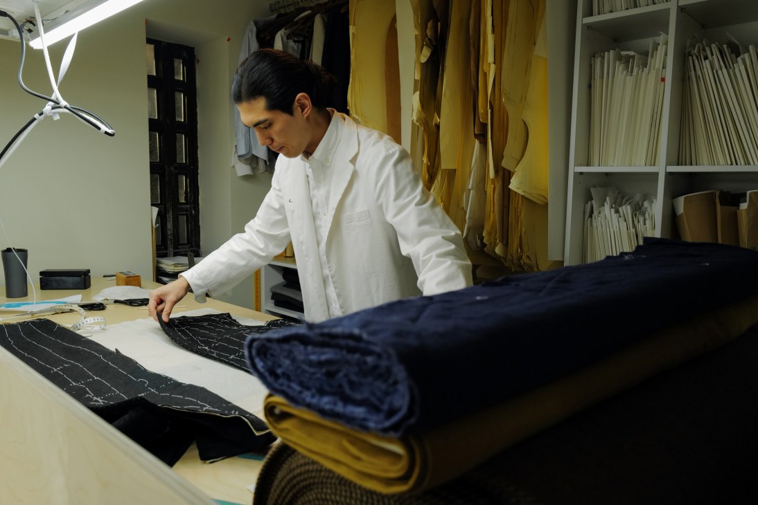 Man in white shirt examining black fabric with pattern pieces on cutting table in tailoring workshop