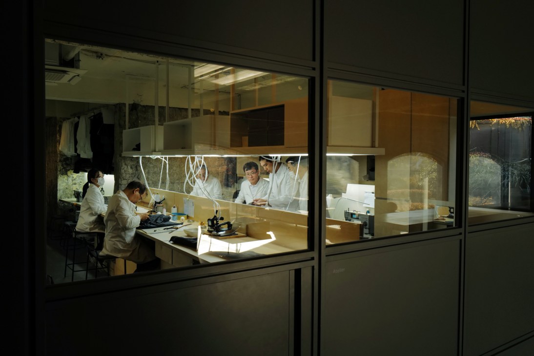Four people in white lab coats working at tables with equipment in a well-lit workshop space viewed through glass