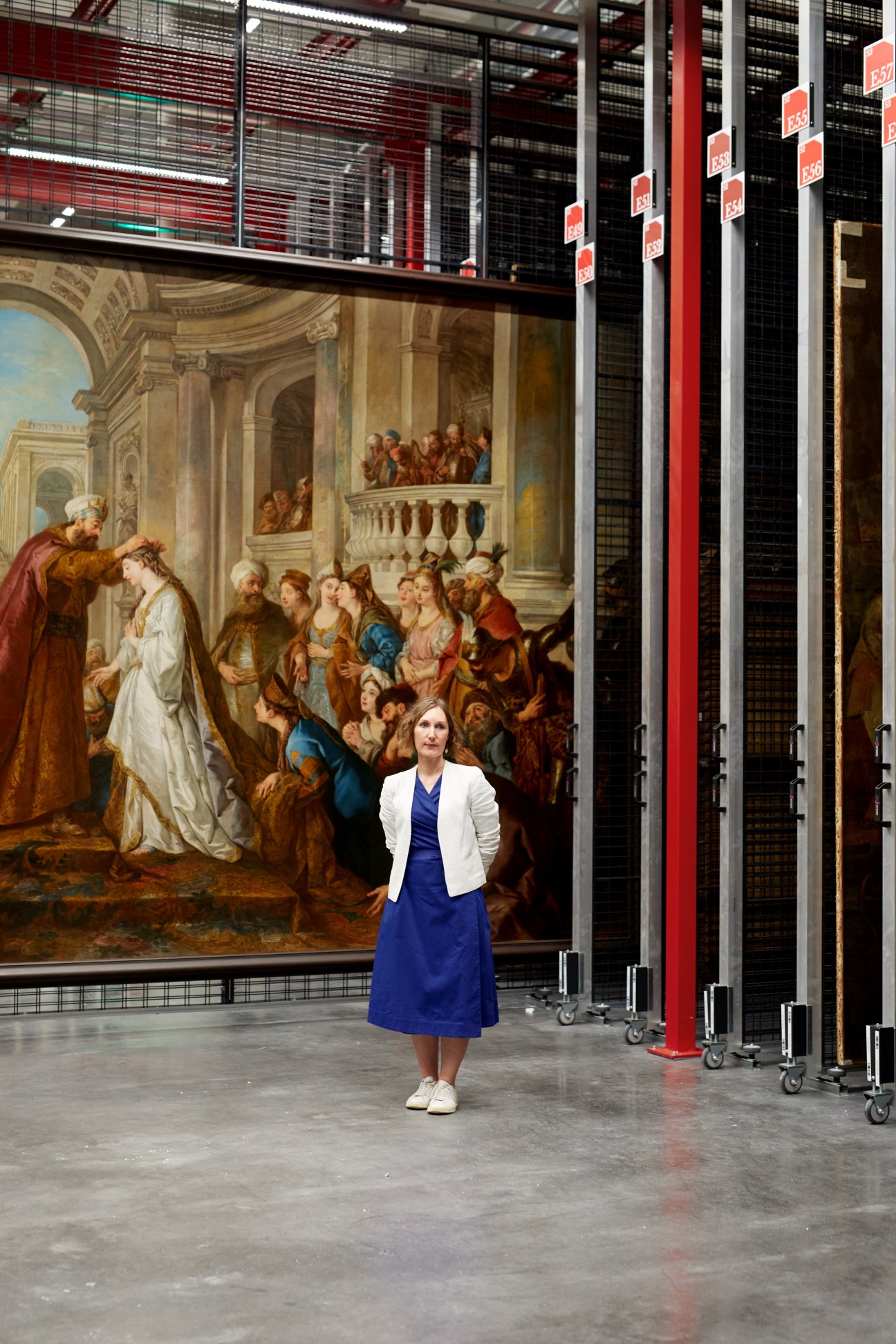 Marie-Lys Marguerite, director of the Louvre Conservation Centre, stands before a large classical painting in a climate-controlled storage facility.