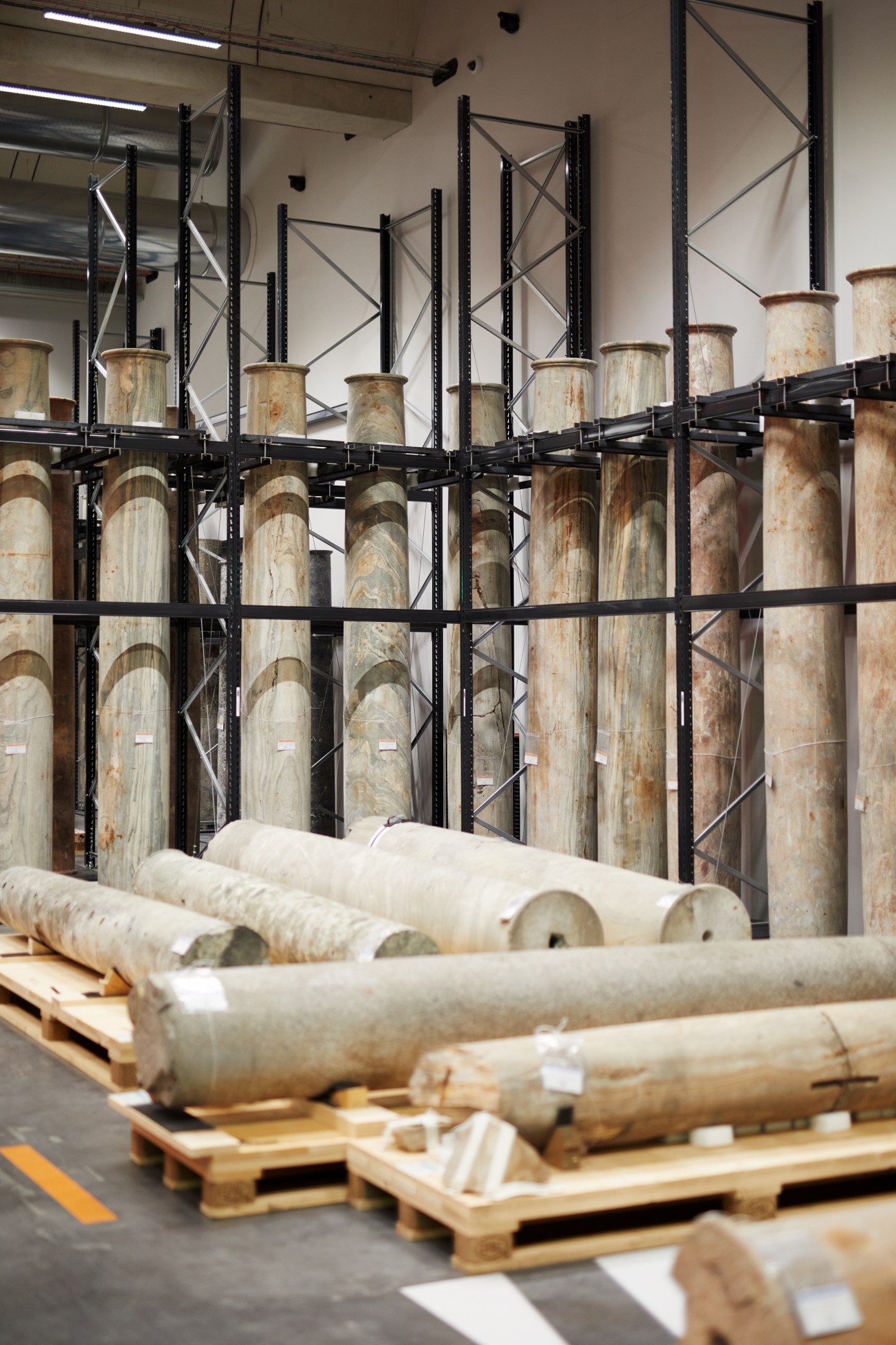 Industrial storage shelving holds ceramic vessels and cylindrical objects on wooden pallets in a climate-controlled facility.