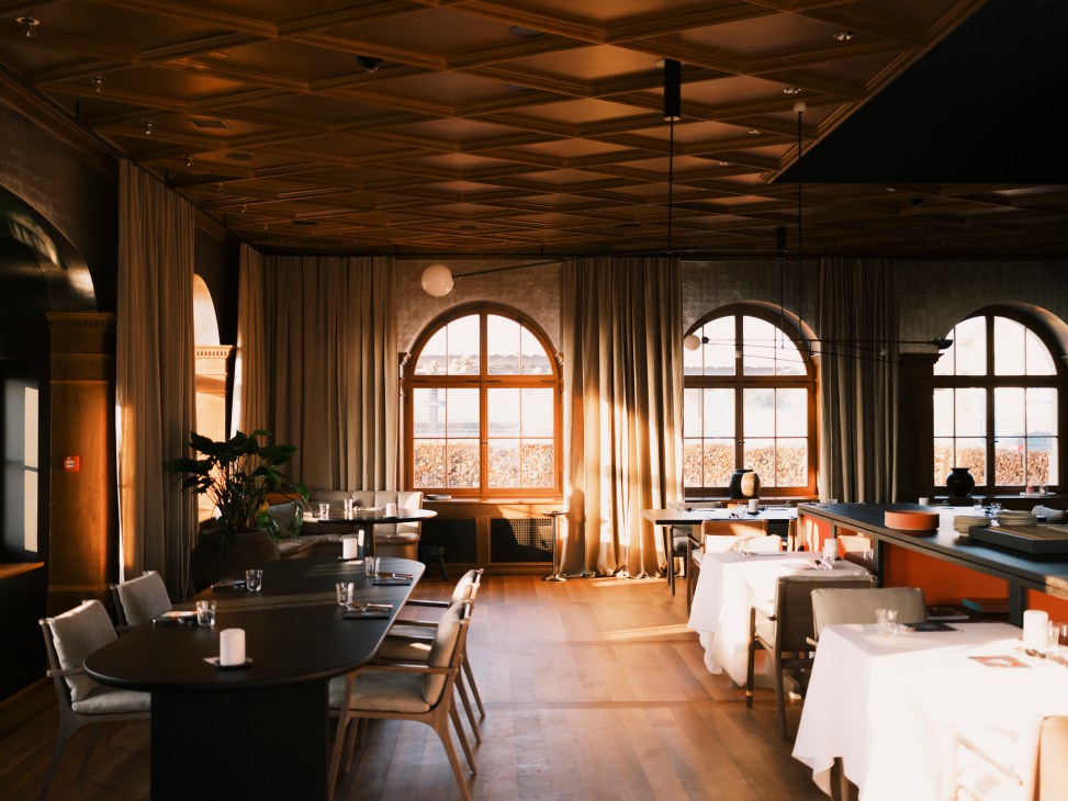 Contemporary restaurant dining room with arched windows, coffered ceiling, round wooden tables and modern chairs
