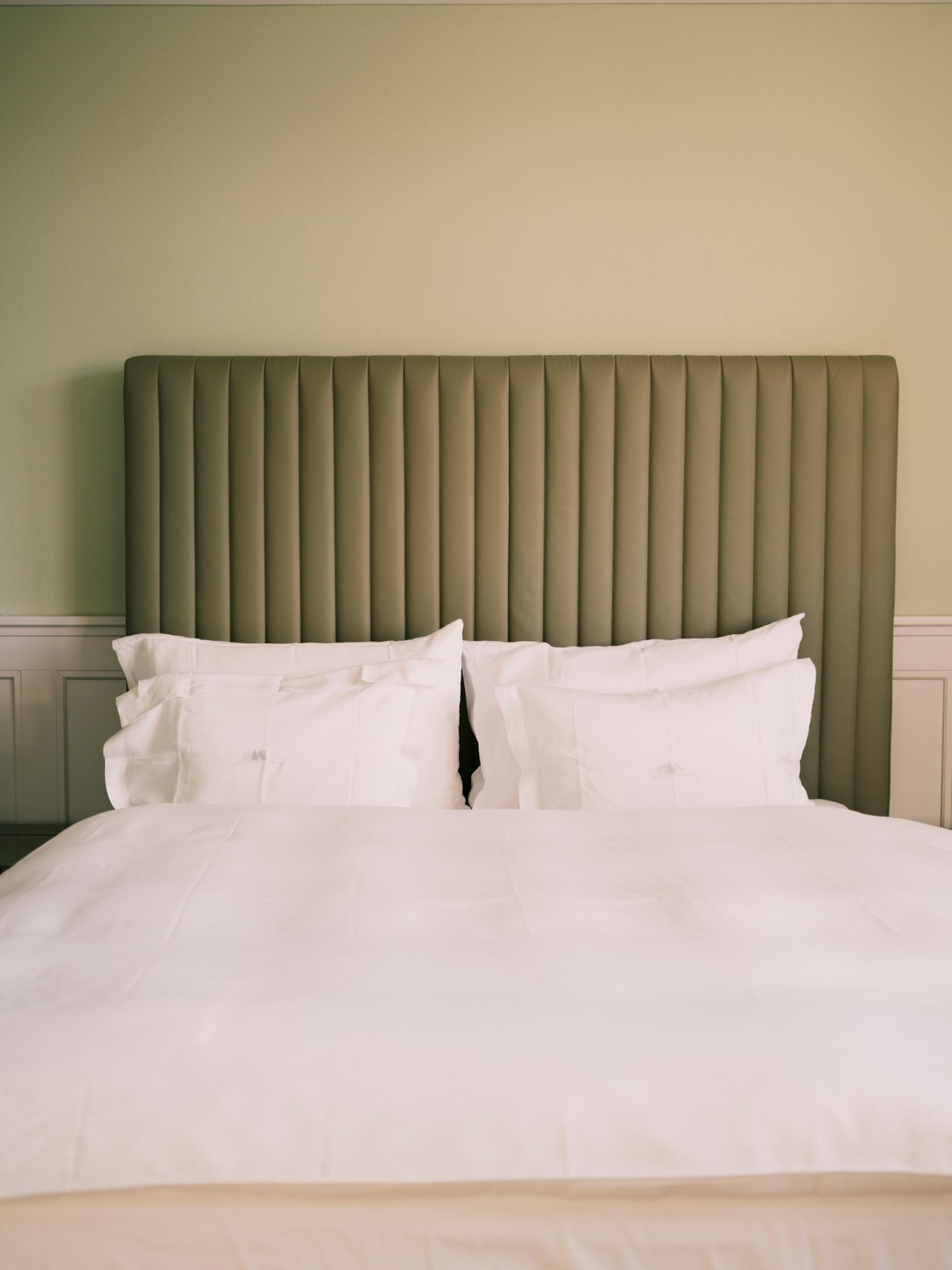 Hotel bedroom with white bedding, olive green fluted headboard, and neutral wall colors