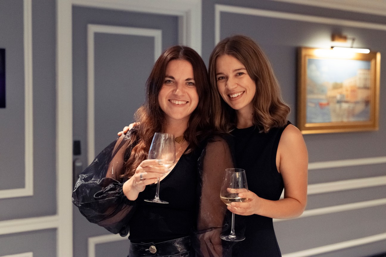 Two women in black outfits holding wine glasses and smiling at Media Summit 2021