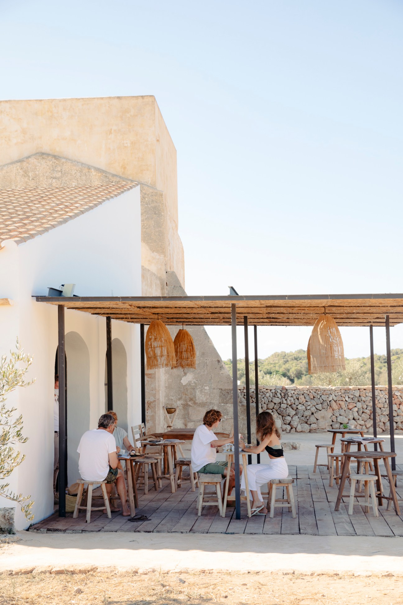 People dining at wooden tables beneath a pergola at a Mediterranean terrace restaurant.