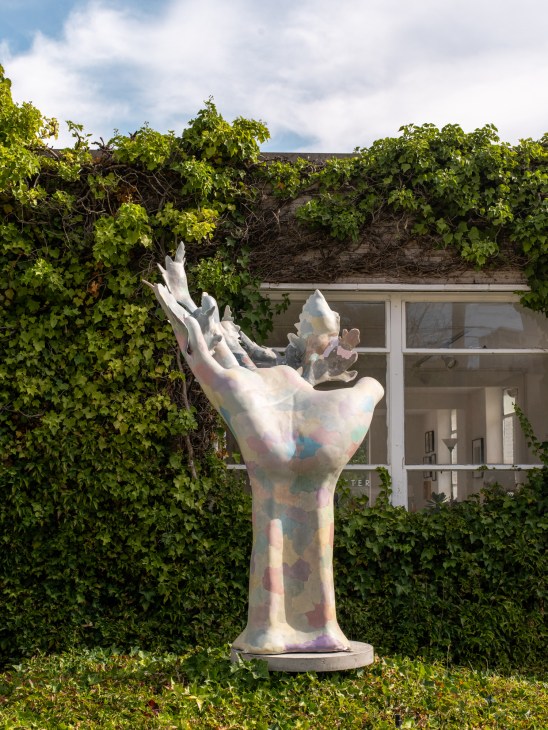 A white sculptural hand installation displayed in front of ivy-covered walls at the Museum of Museums in Seattle.