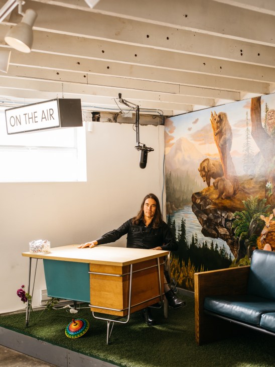 Greg Lundgren at the Museum of Museums in Seattle, standing in a studio space with a microphone setup and vintage desk.