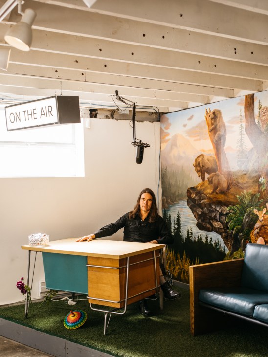 Greg Lundgren at the Museum of Museums in Seattle, standing in a studio space with a microphone setup and vintage desk.