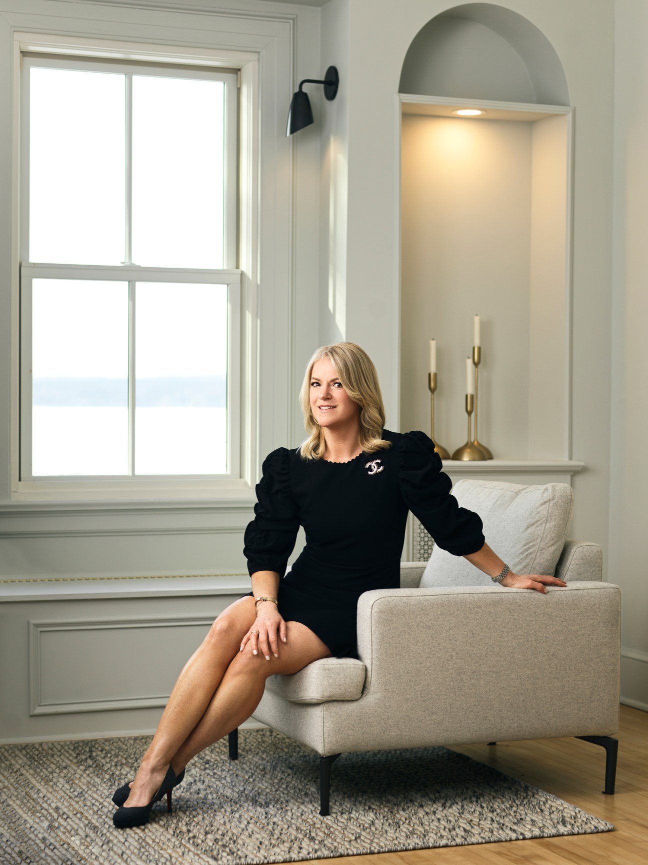 Pamela Mullinger sitting in a beige armchair wearing a black dress in an elegant white room