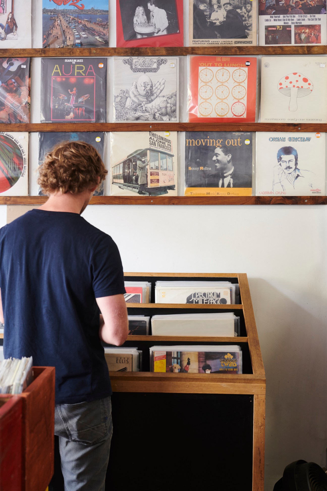 Person browsing vinyl records displayed on wooden shelving at Neighbourhood Books.