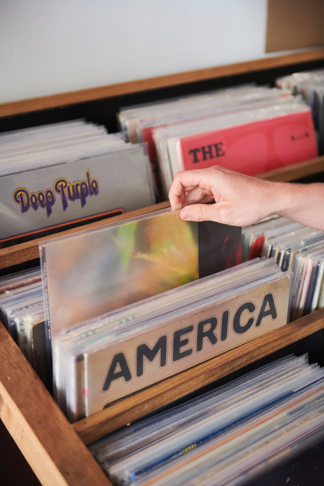 A hand browsing vinyl records organized alphabetically by artist in wooden bins at a record store.
