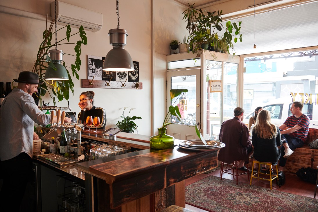 Interior of Low Key bar with customers seated at tables and a barista behind the counter decorated with hanging plants.