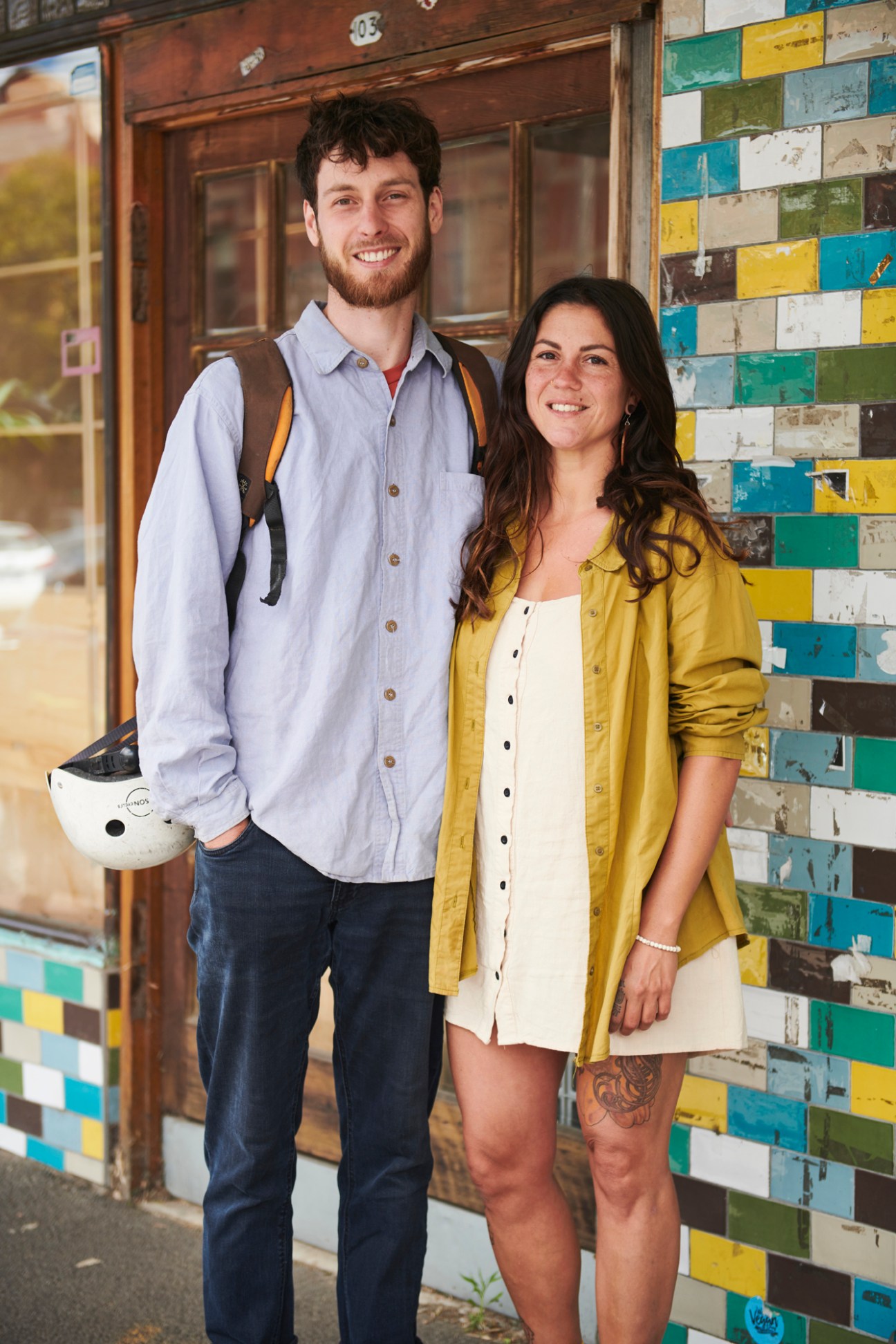 Two people smiling in front of a colourful tiled wall on a Melbourne street.